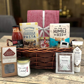Gourmet anniversary gift basket with a blanket, pasta, sauce, crackers, a candle, lotion, caramels, and more