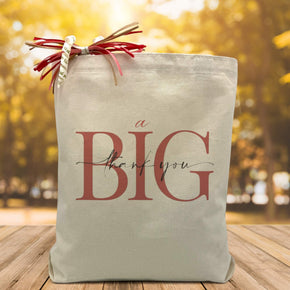 A big thank you printed on a canvas tote bag sitting on a wood table with a blurred fall background.
