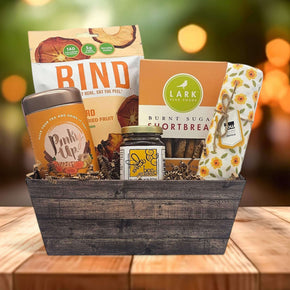 Gourmet Fall Gift Basket that has fruit chips, tea, cookies, honey and dishtowel sitting on a table