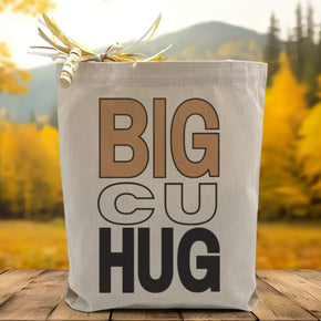 A big cu hug text beige and black colors  on a canvas tote bag placed on a wood table with woodsy background. 