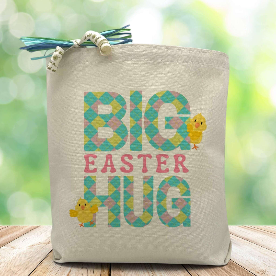 A pink, blue and yellow plaided big easter hug text on a canvas tote bag placed on a wood table with blurred green background.