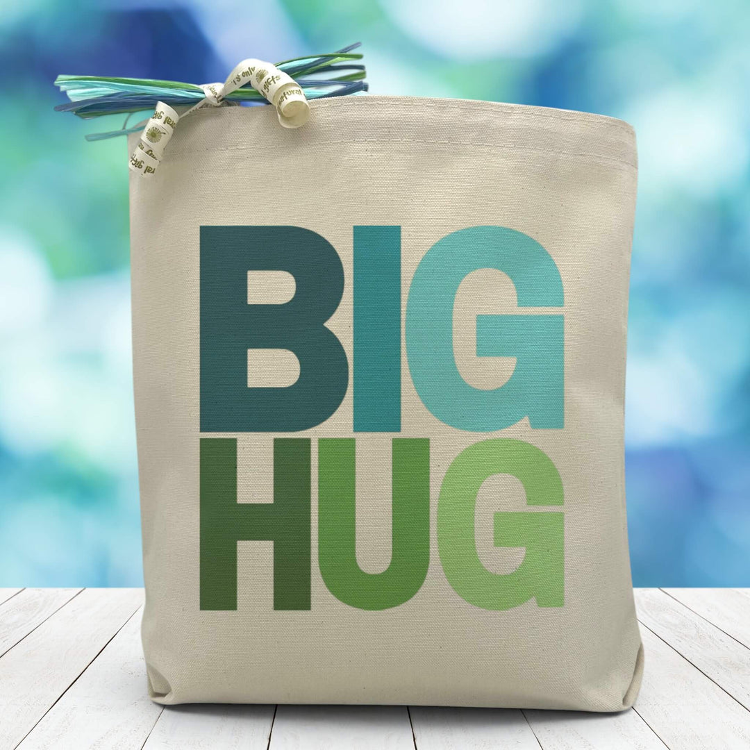 A blue and green big hug text on a canvas tote bag placed on a wood table with blurred blue background.
