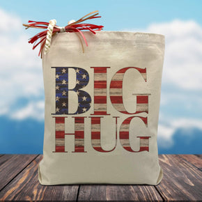 A untied states flag filled text on a canvas tote bag placed on a wooden table with mountains in the background.