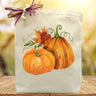 Two orange whimsical pumpkins printed on a canvas tote bag sitting on a table with a fall background