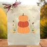 3 pumpkins stacked on top of each other printed on a canvas tote bag sitting on a table