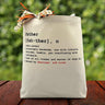 A text stating the definition of a father with a chance to add adored by custom name on a canvas tote bag placed on a wooden table with a leafy background.