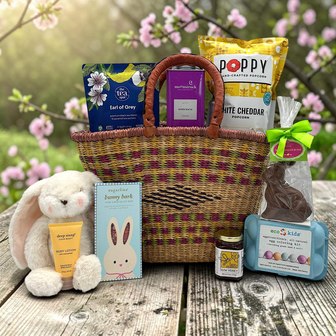handwoven basket with tea, cocoa, popcorm a stuffed bunny, lotion, chocolate bar, honey, egg coloring, and chocolate bunny