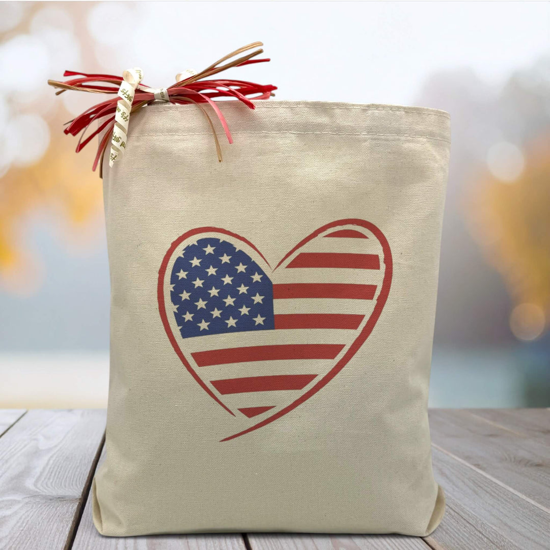 A American Flag filled heart on a canvas tote bag, placed on a wooden table with a blue blurred background.