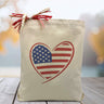 A American Flag filled heart on a canvas tote bag, placed on a wooden table with a blue blurred background.