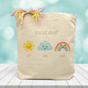 A Forecast ahead baby inspired image, with a sun, cloud, and rainbow saying eat, sleep, poop. Printed on canvas tote bag placed on wooden table with blue blurred background 