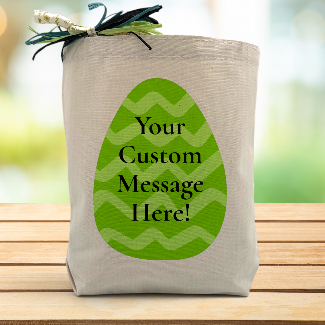 A Green easter egg with a chance to add a custom message in the middle printed on a canvas tote bag, placed on a wooden table and a leafy background.