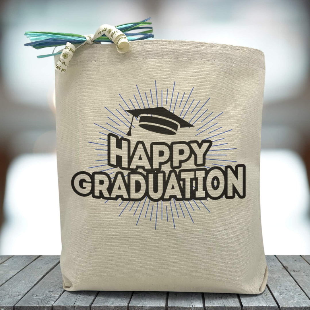 A text saying happy graduation in all black with a graduation cap printed on a canvas tote bag, set on wooden table with a grey blurred background.