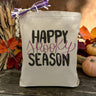 A text saying happy spooky season with only the word spooky being purple printed on a canvas tote bag, set on a wooden table with a fall inspired background.