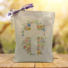 A Easter inspired cross with a floral background printed on a canvas tote bag  set on a wooden table with a light filled forest background.