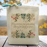 A floral background with the text may memories ease your sorrow and may time bring you peace printed on a canvas tote bag set on a wooden table.