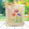 a light rainbow box with the text our thoughts are with you placed inside, along with three poppies, printed on a canvas tote bag set on a wooden table.