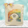 A rainbow water colored background with a text saying part of my heart is at the rainbow bridge with a paw print underneath printed on a canvas tote bag.
