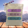 a black text saying rest, relax and recover with each of the words placed in a different color bar being purple light purple and blue printed on a canvas tote bag, 