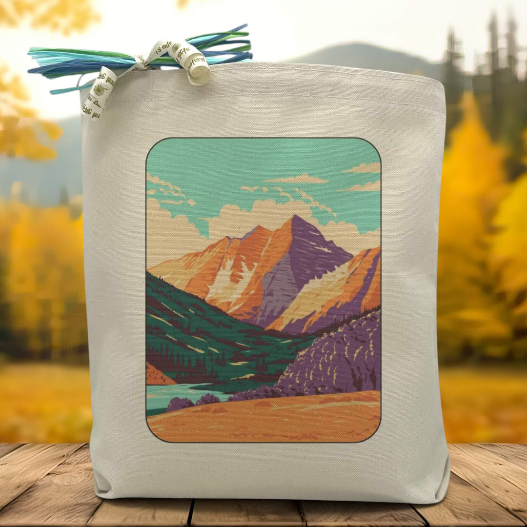 A picture of the rocky mountain high mountains printed on a canvas tote bag placed on a wooden table with a tree filled background.
