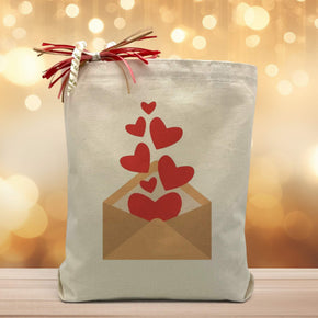 a envelope with hearts floating out of it indicating that you are sending love printed on a canvas tote bag placed on a wooden table with a light filled background. 