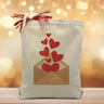 a envelope with hearts floating out of it indicating that you are sending love printed on a canvas tote bag placed on a wooden table with a light filled background. 