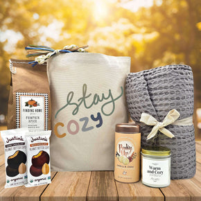 Stay cozy gift basket with pancake mix, 2 justin peanut butter cups, tea, a large candle and a blanket