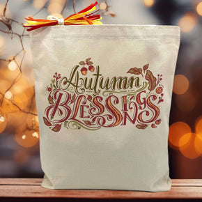 Autumn Blessings with leaves printed on canvas tote bag sitting on a table with a blurrred fall background