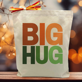 BIG HUG printed in oranges and greens on canvas tote bag sitting on a table with a blurred fall background