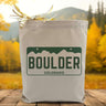 A green boulder colorado sign placed on a canvas tote bag with a woodsy background.