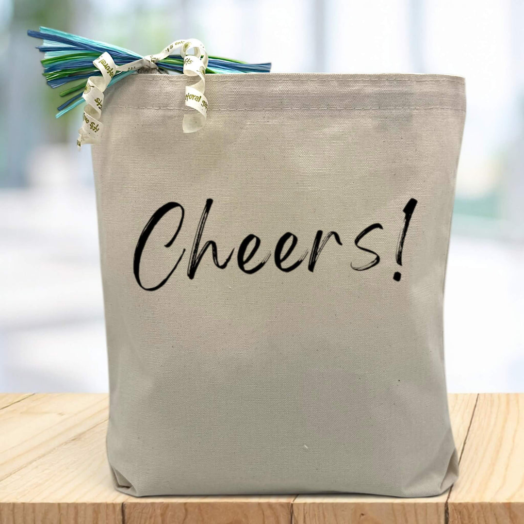 Cheers! in black printed on canvas tote bag sitting on table with white blurred background