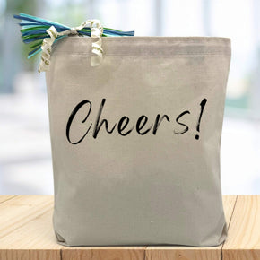 Cheers! in black printed on canvas tote bag sitting on table with white blurred background