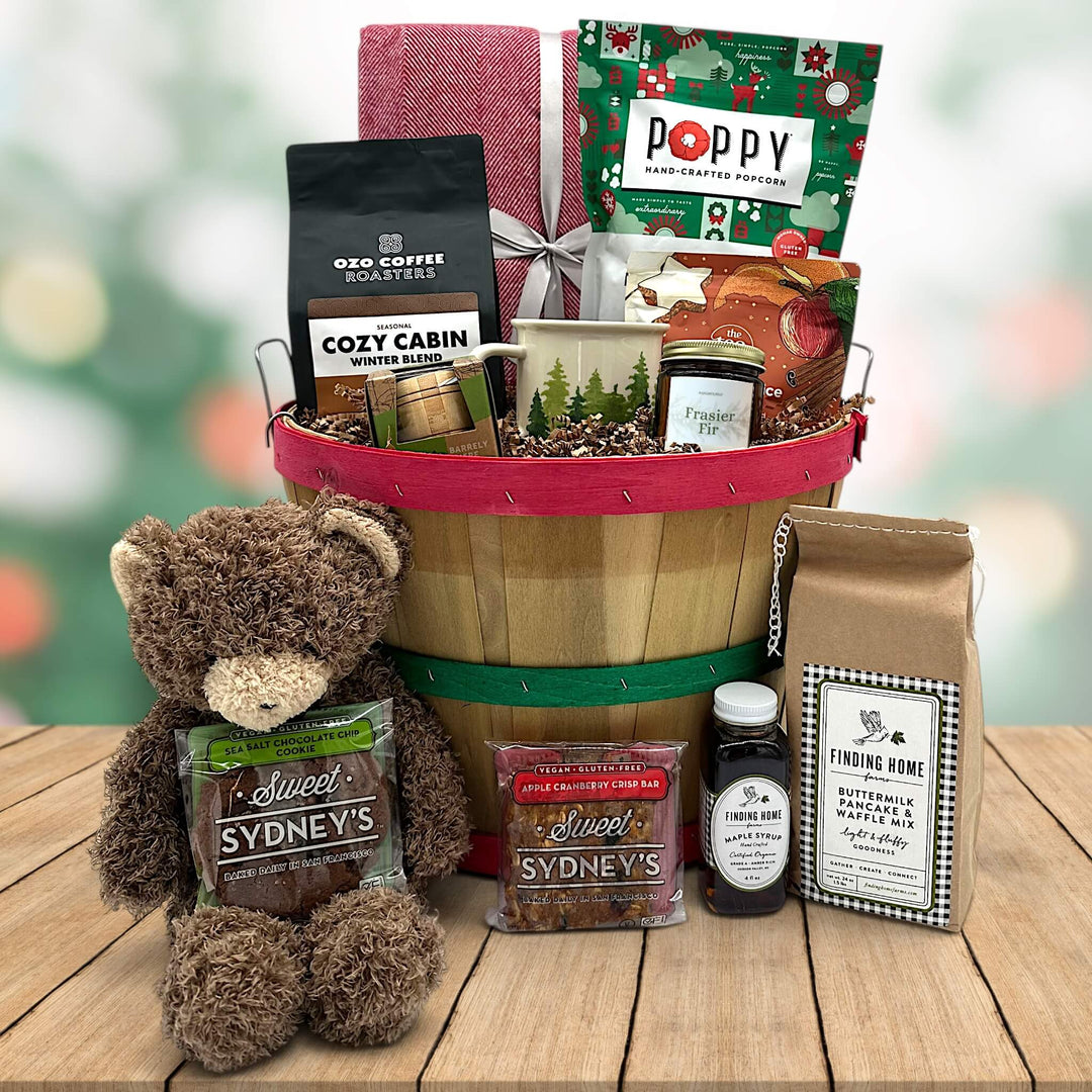 Gourmet christmas gift basket with a blanket, popcorn, coffee, a mug, tea, a puzzle, pancake and syrup, cookies and a stuffed bear.