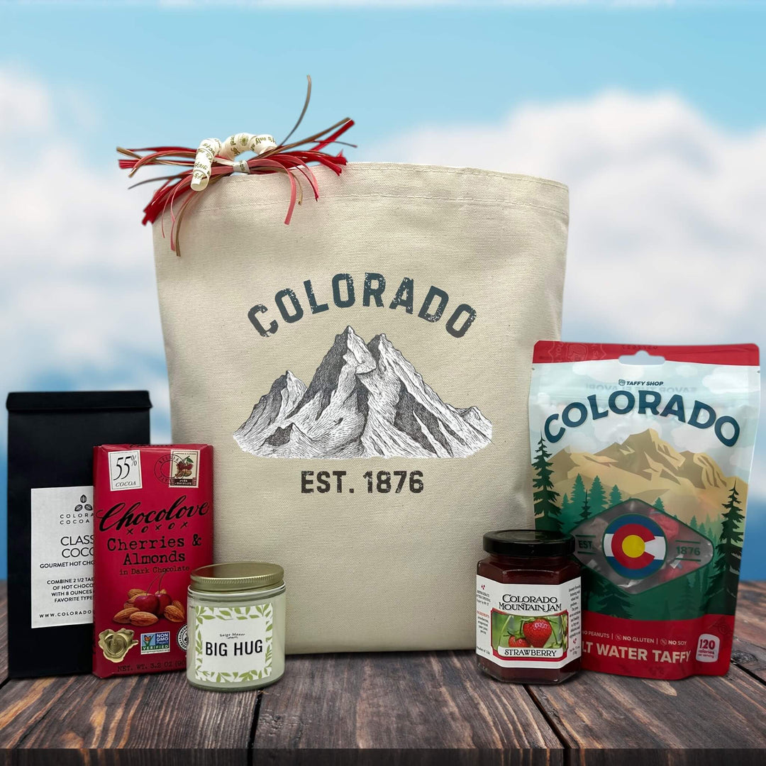 CO Est 1876 printed on tote sitting on table with cocoa, chocolate, candle, jam and colorado taffy
