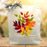 Colorful fall leaves printed on a canvas tote bag sitting on a table with a fall background