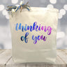 Canvas gift bag with thinking of you text in blue and purple watercolor script on a wooden surface