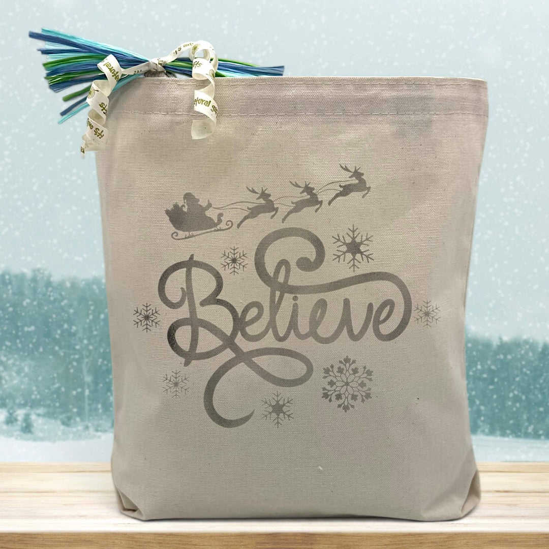silver believe printed on a canvas tote bag sitting on a wood table with a snowy background