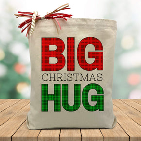 red and green plaid big christmas hug printed on a canvas tote bag sitting on a wood table