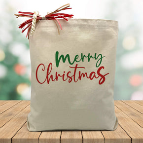 red and green merry christmas printed on a canvas tote bag sitting on a wood table
