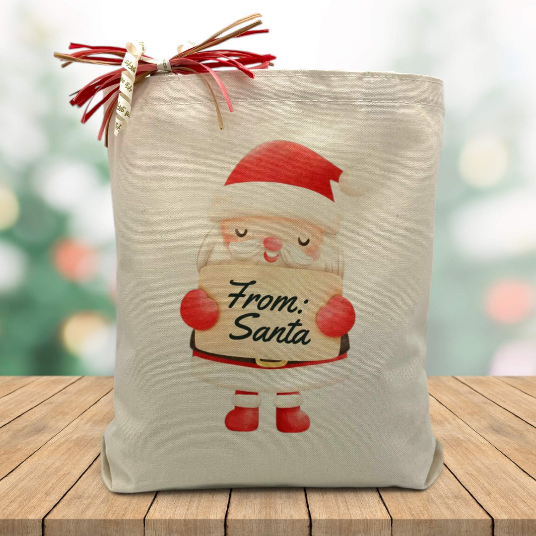 santa claus holding a from santa sign printed on a canvas tote bag sitting on a wood table