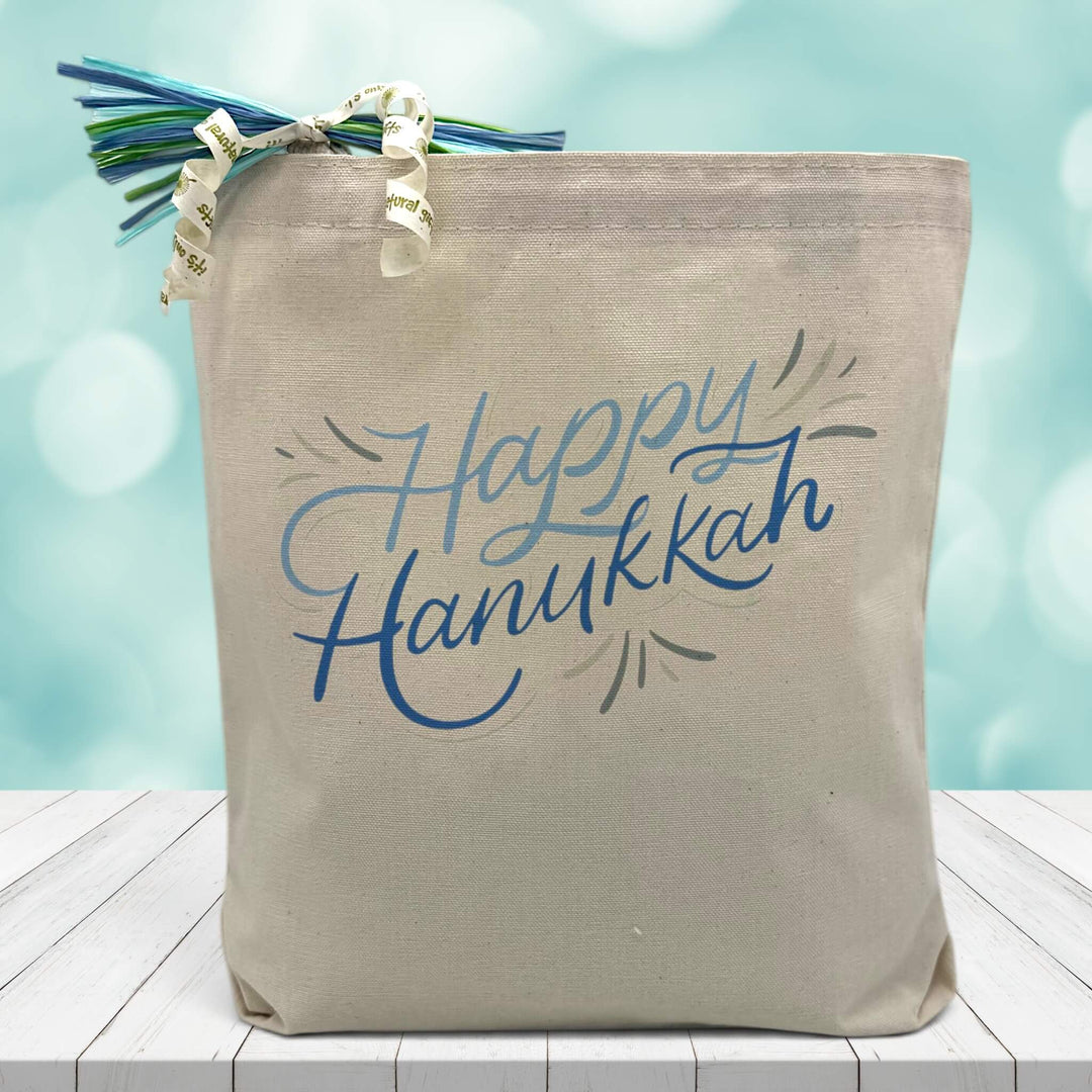 blue happy hanukkah printed on a canvas tote bag sitting on a table with a blurred blue background