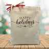happy holidays printed on a canvas tote bag sitting on a wood table with a holiday blurred background