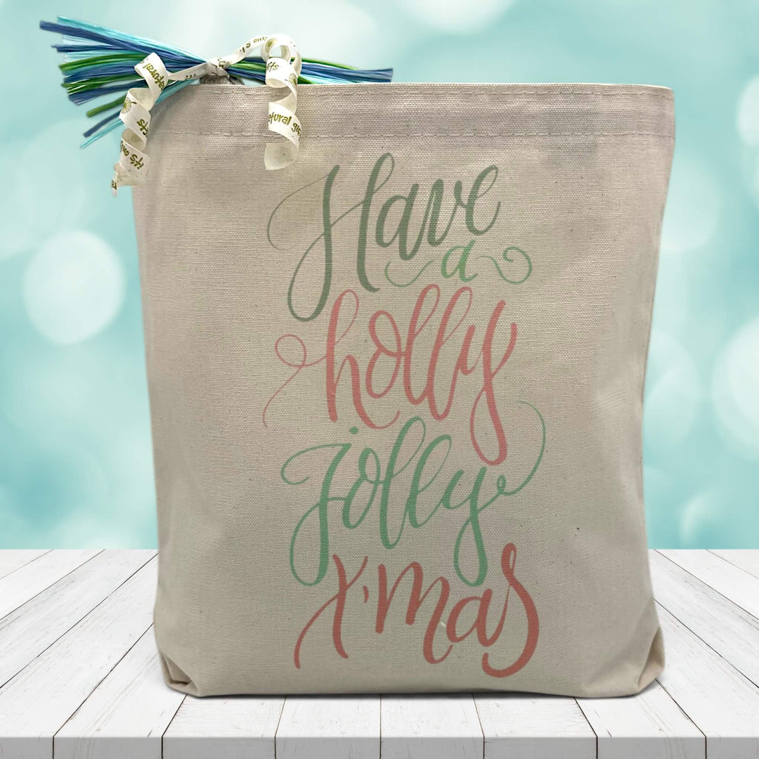 have a holly jolly xmas printed in red and green on a canvas tote bag sitting on a wood table with a blurred blue background