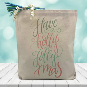have a holly jolly xmas printed in red and green on a canvas tote bag sitting on a wood table with a blurred blue background