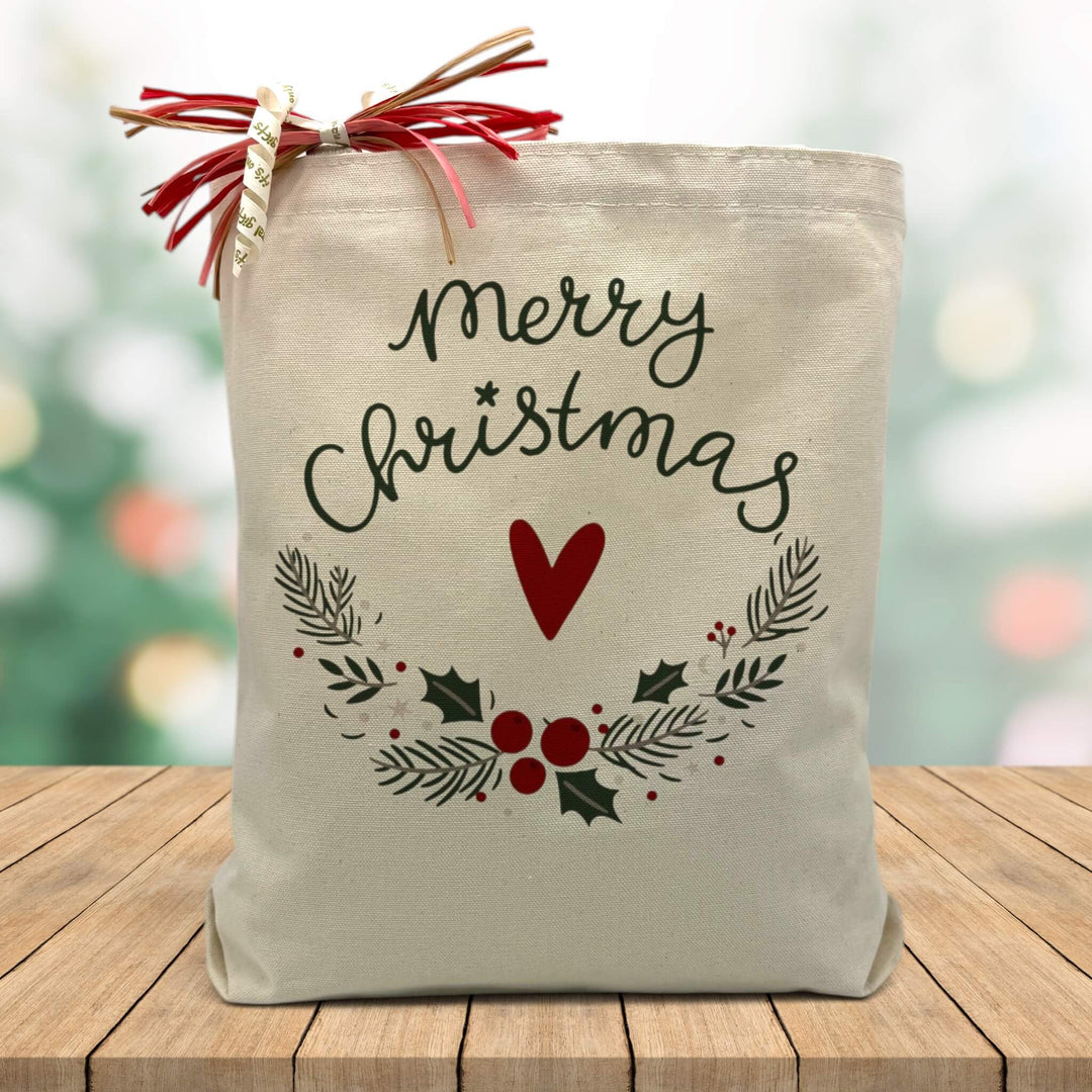 Merry christmas with a heart and wrath printed on a canvas tote bag sitting on a wood table