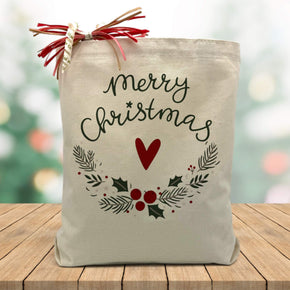 Merry christmas with a heart and wrath printed on a canvas tote bag sitting on a wood table