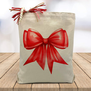 large red gifting bow printed on a canvas tote bag sitting on a wood table with a white blurred background