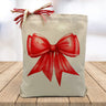 large red gifting bow printed on a canvas tote bag sitting on a wood table with a white blurred background