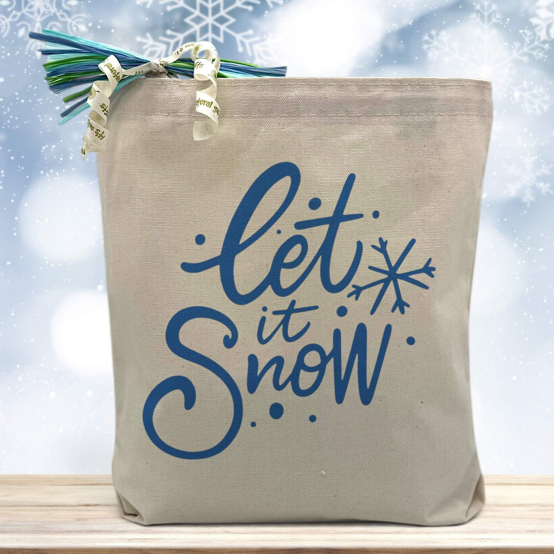 let is snow in blue printed on a canas tote bag sitting on a table with a snowflake background