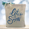 let is snow in blue printed on a canas tote bag sitting on a table with a snowflake background