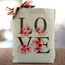 love with flowers printed on a canvas tote bag sitting on a table with a blurred white background